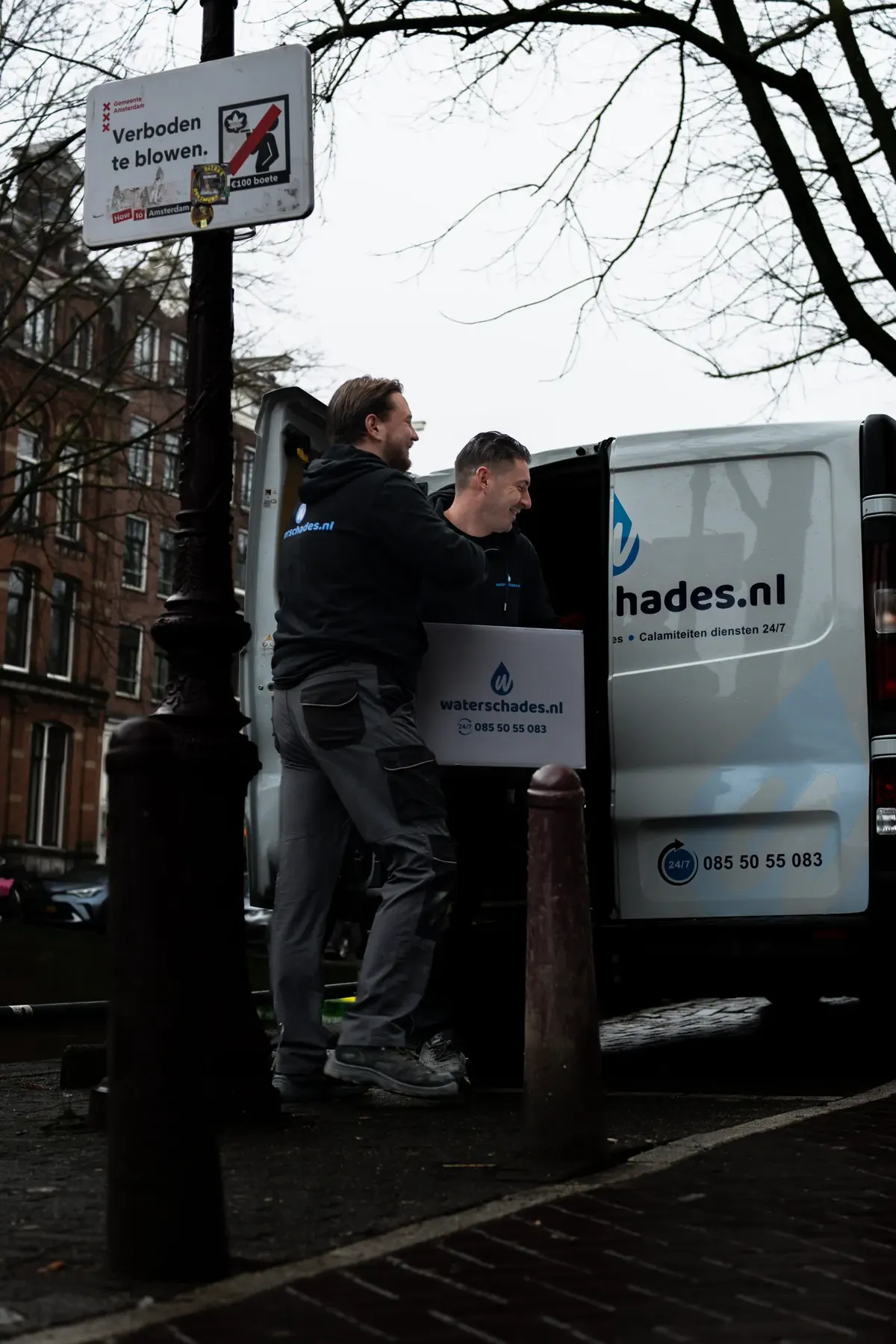 Twee medewerkers laden apparatuur uit de servicebus in een Amsterdamse straat